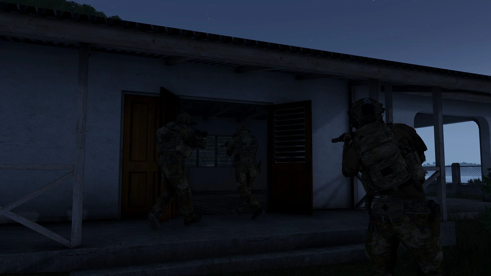 Military soldiers entering a house at night, armed and wearing camouflage gear.