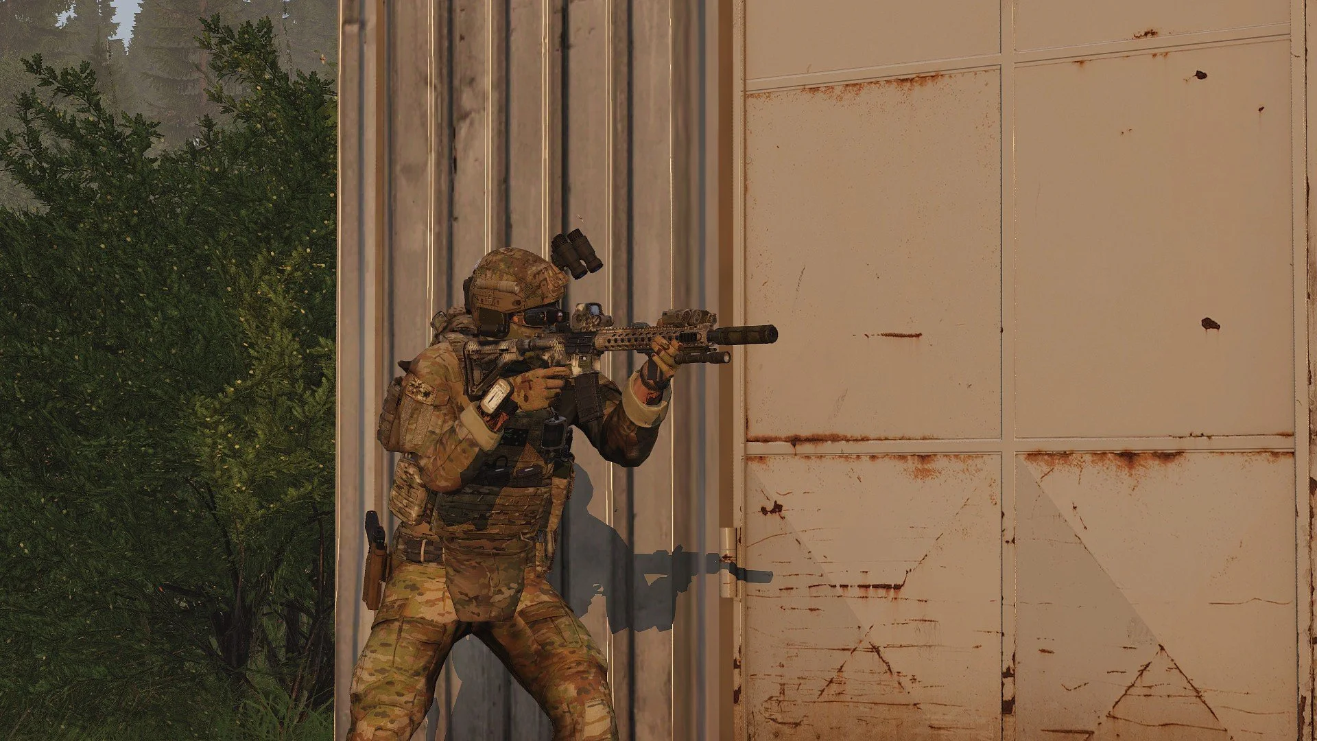A soldier in camouflage gear aiming a rifle while crouching behind a metal wall, with green trees visible in the background.