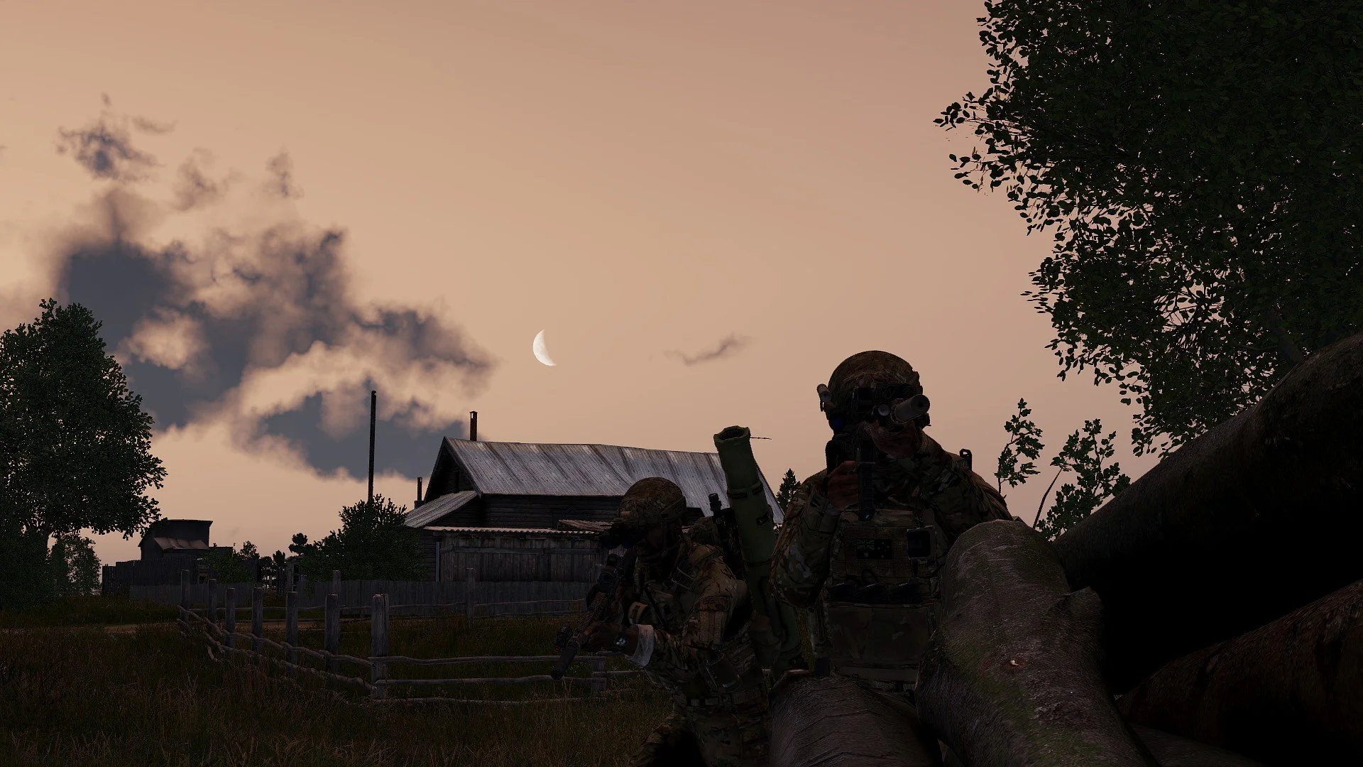 Silhouettes of two soldiers in camouflage gear and helmets standing outdoors near fallen tree logs, with trees, a wooden fence, and a house in the background during sunset or dusk