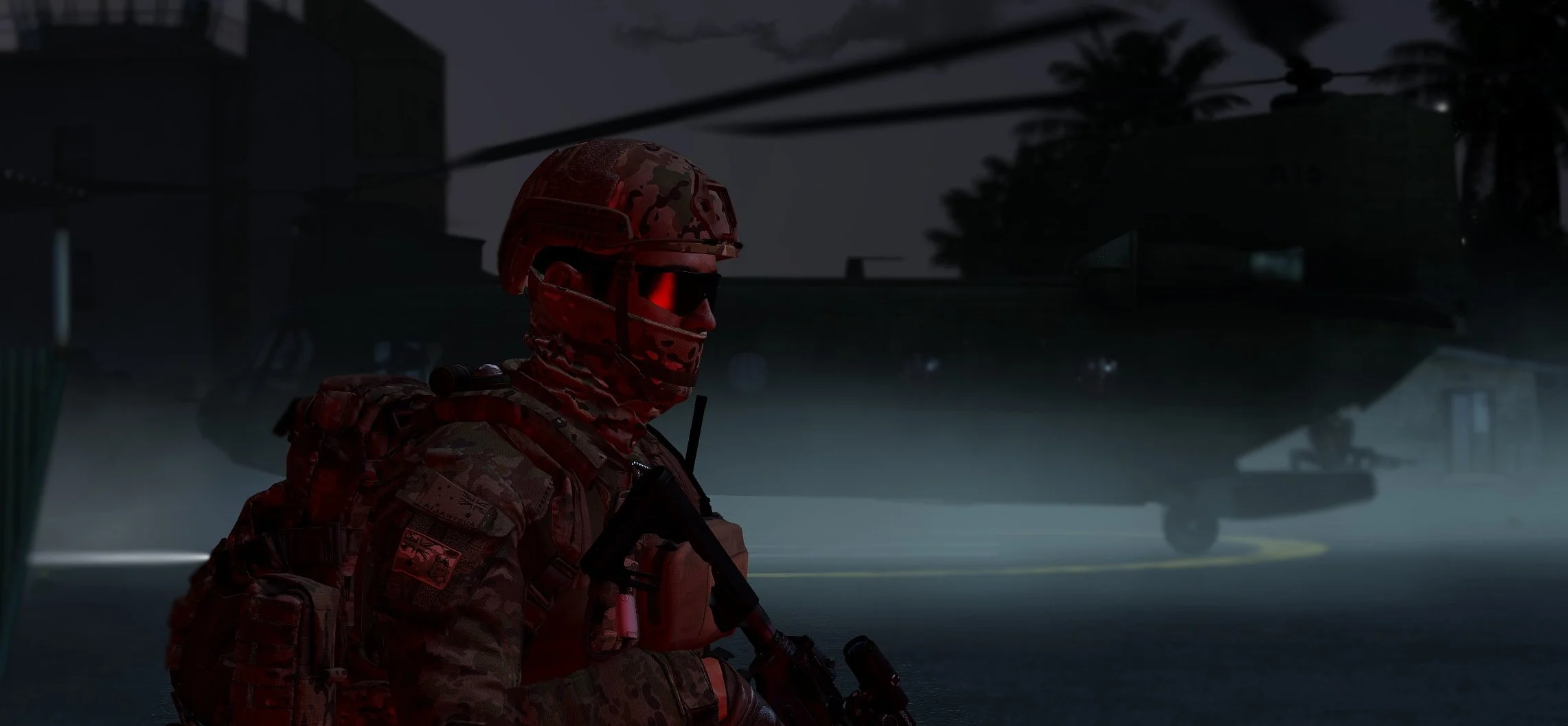 A soldier in camouflage uniform with a helmet and tactical gear, sitting on the ground during nighttime, with a large military helicopter in the background.